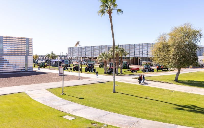 Birds eye view of the Arizona Western Yuma campus during the 2025 Agriculture Summit, looking down at the 3C building, palm trees, and sidewalks, with large tractors and agriculture equipment parked in the green space.