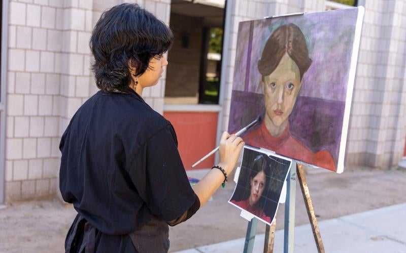 Student holds a paintbrush over a painting.