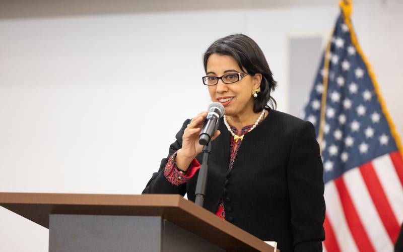 Reetika Dhawan speaks at a podium with an American flag behind her.