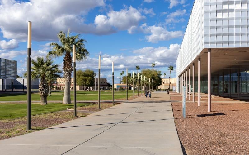 Looking up the path on the AWC campus, with the AS building to the right. Blue sky with clouds and palm trees.