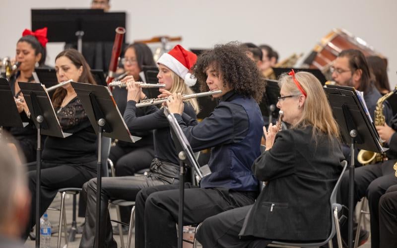 Members of the AWC Community Band perform in the 2023 Christmas Concert. Some are wearing Santa hats and red bows.