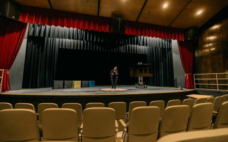 Single person stands on stage addressing an empty theater
