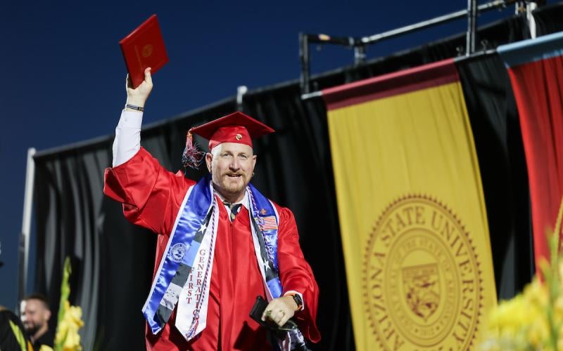 Veteran AWC student raises his diploma in the air while he walks across the stage at commencement.