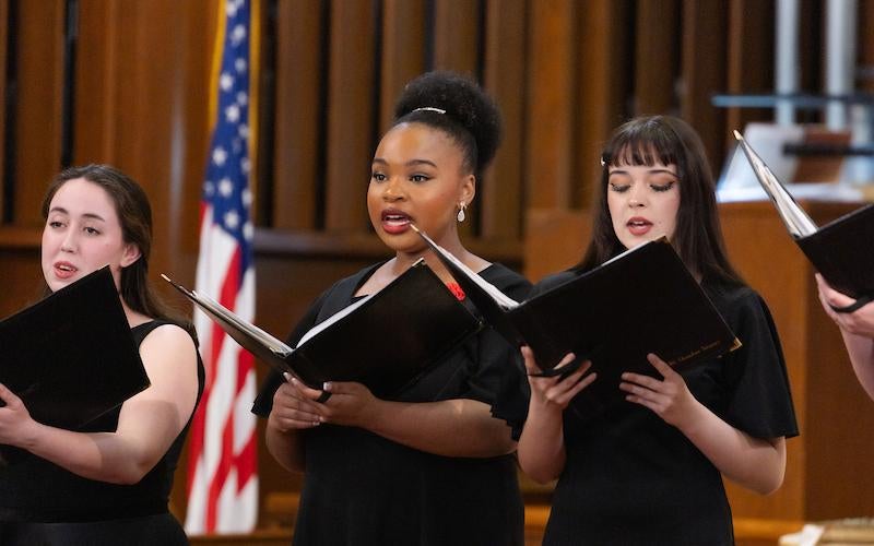 Three choir girls hold music books and sing