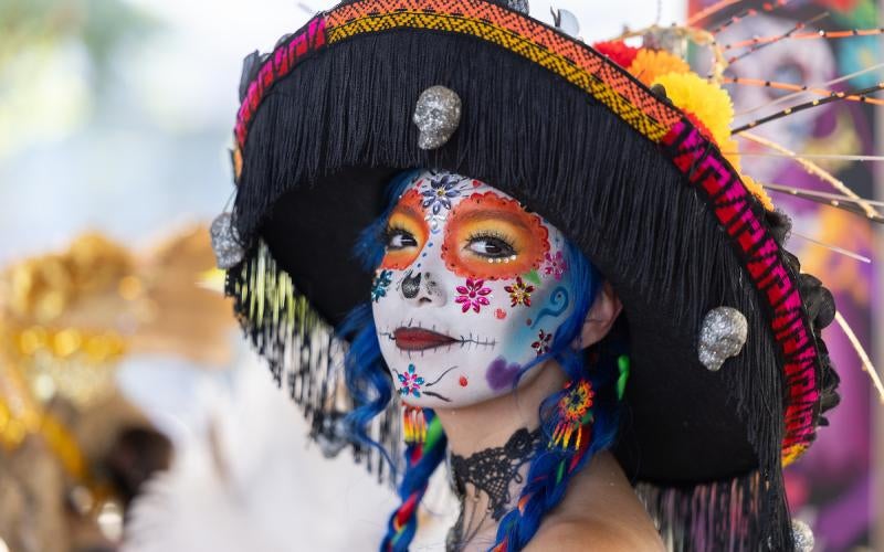 Girl dressed in a Catrina costume with face paint and a wide-brimmed fringe hat. 