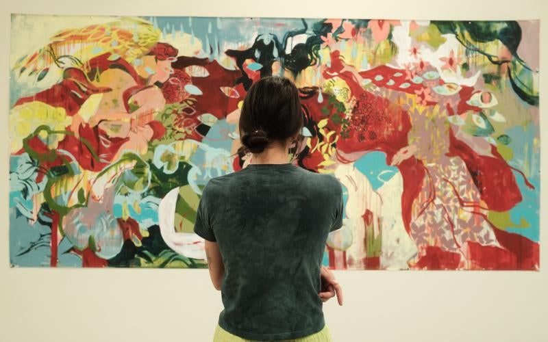 A woman stands facing a colorful abstract painting.