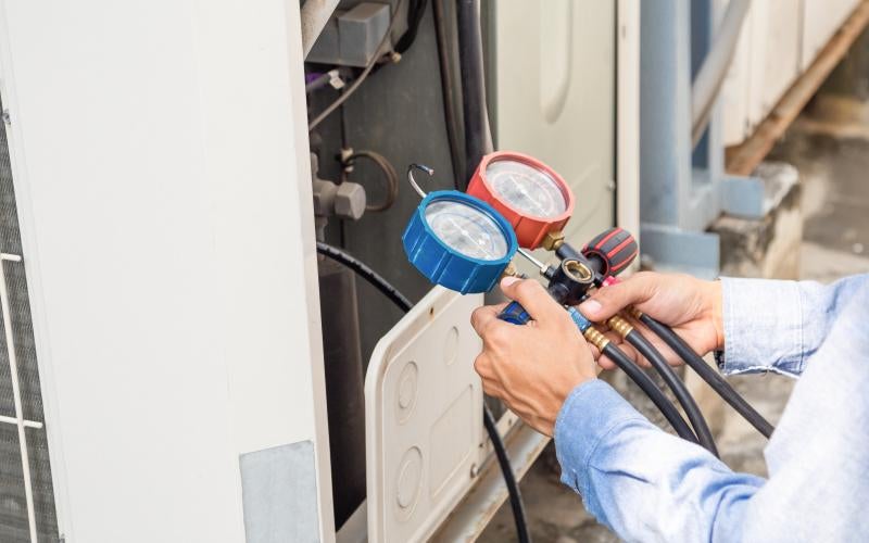 HVAC technician holds a set of gauges, one blue and one red.