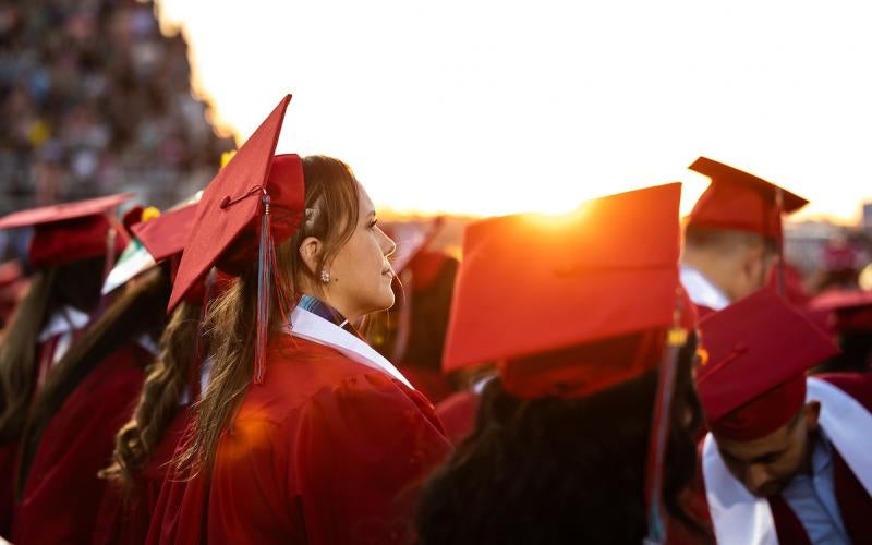 Graduates wearing caps and gowns while the sun sets at Veterans Memorial Stadium at the 2024 Commencement.