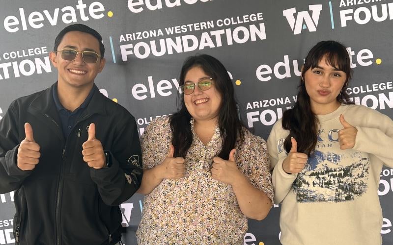 Students stand in front of an AWC Foundation banner with thumbs up.