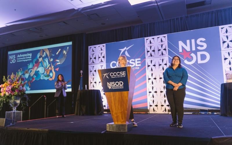 Dr. Courtney Adkins announces Saghey Barcenas as the winner of the 2026 NISOD Student Graphic Design Contest. Her design is displayed in the back left.