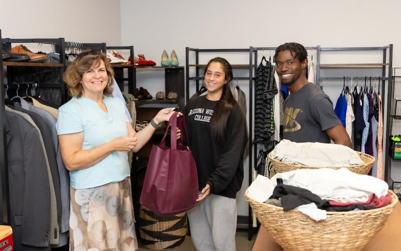 AWC staff member passes a grocery bag to two students in The Cubby closet at AWC.